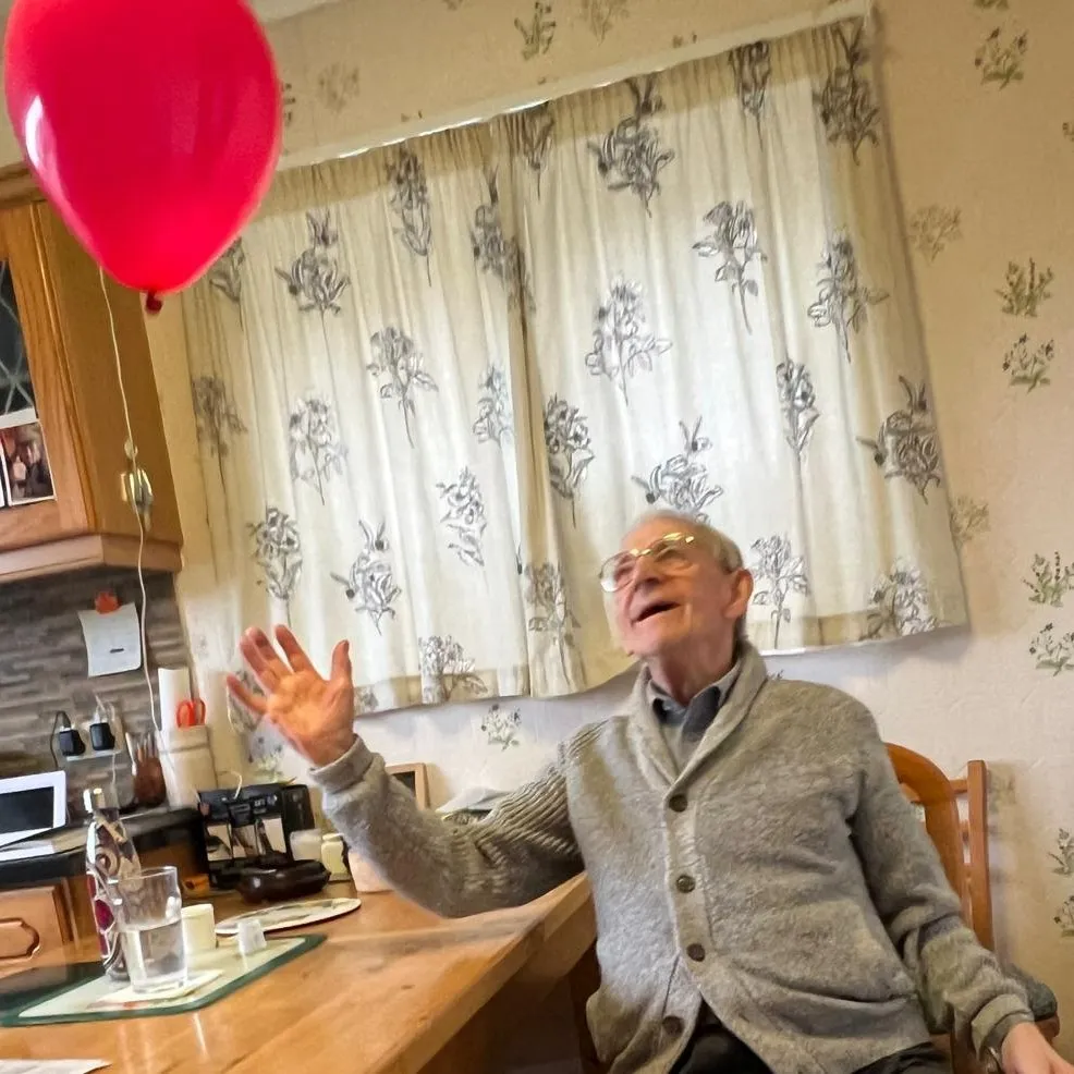 A man sitting at a table with a red balloon in the air.