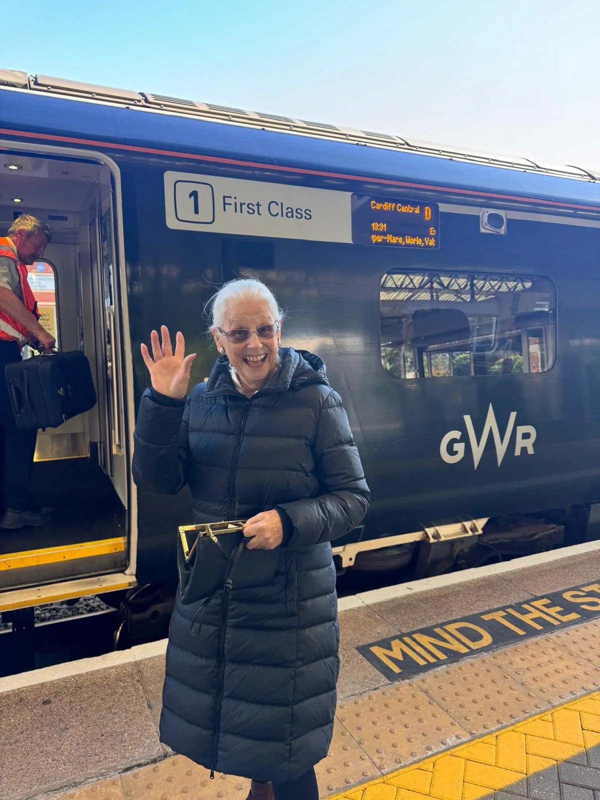 A woman waves as she stands in front of a train.