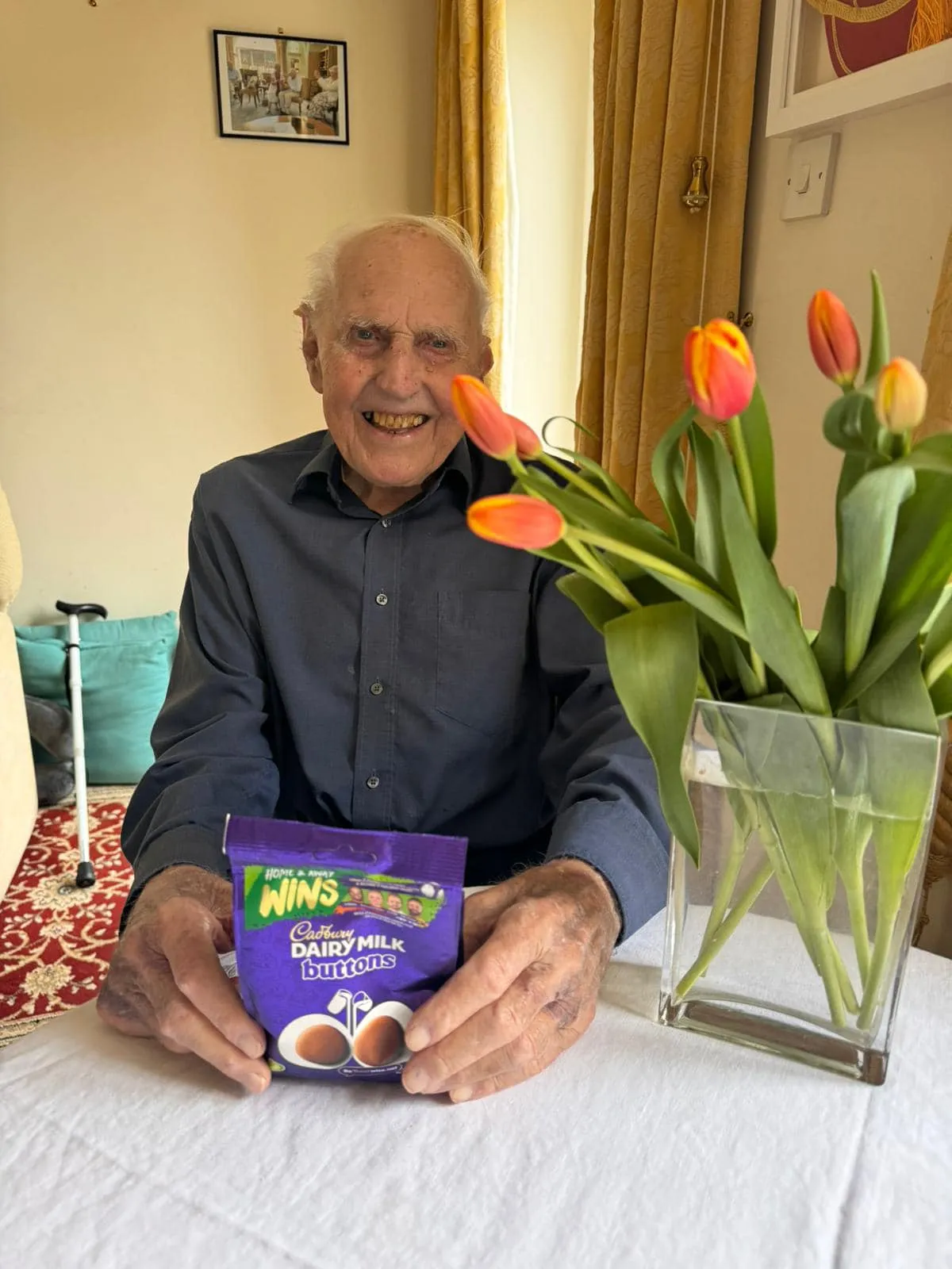 A man sitting at a table with a box of caddy and a vase of.