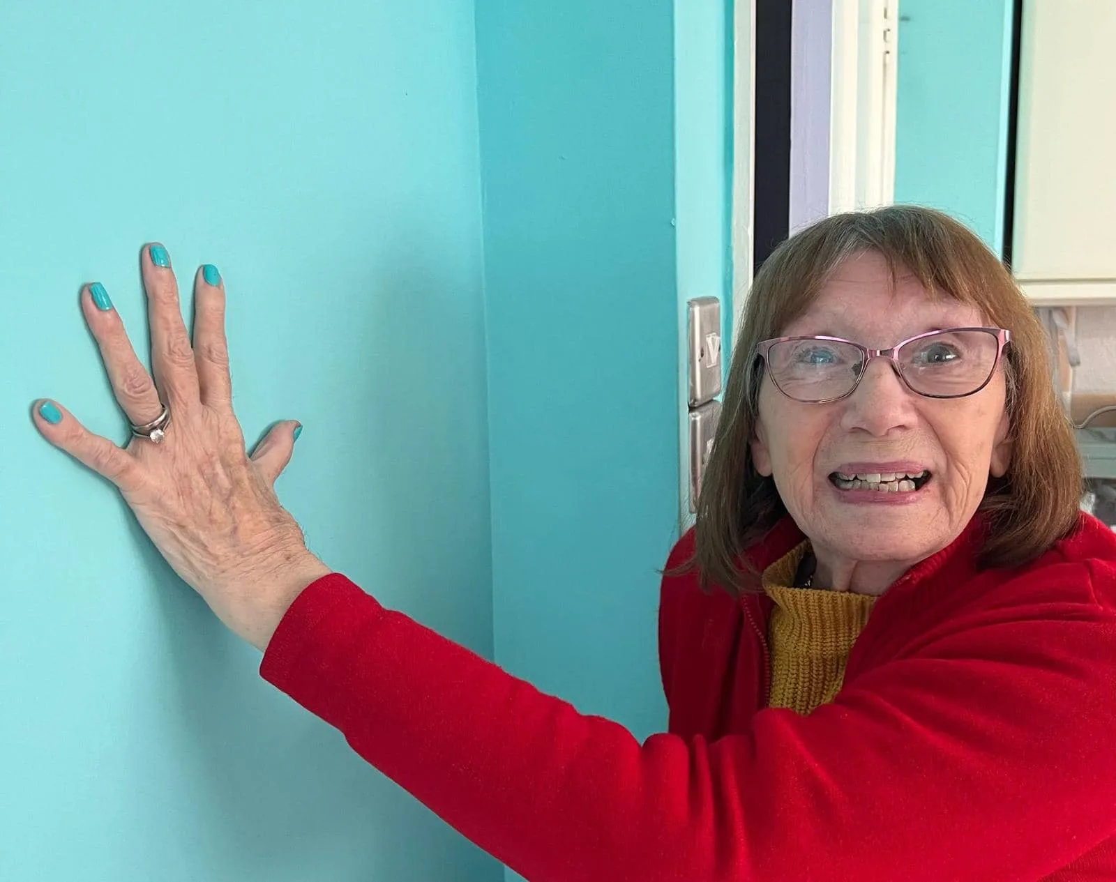 A woman in a red sweater is touching a blue wall.